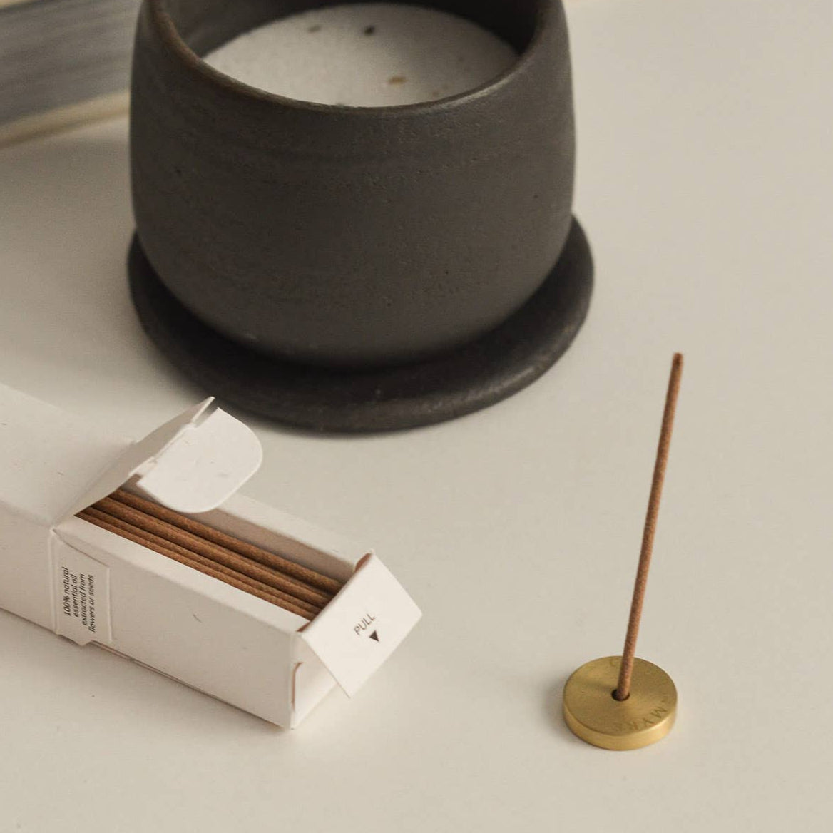 Incense stick holder with a lit incense stick next to a box of incense sticks on a light surface.
