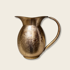 Gold brass jug on a light beige backdrop