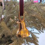 Gold bell ornament hanging from a branch on a wooden surface