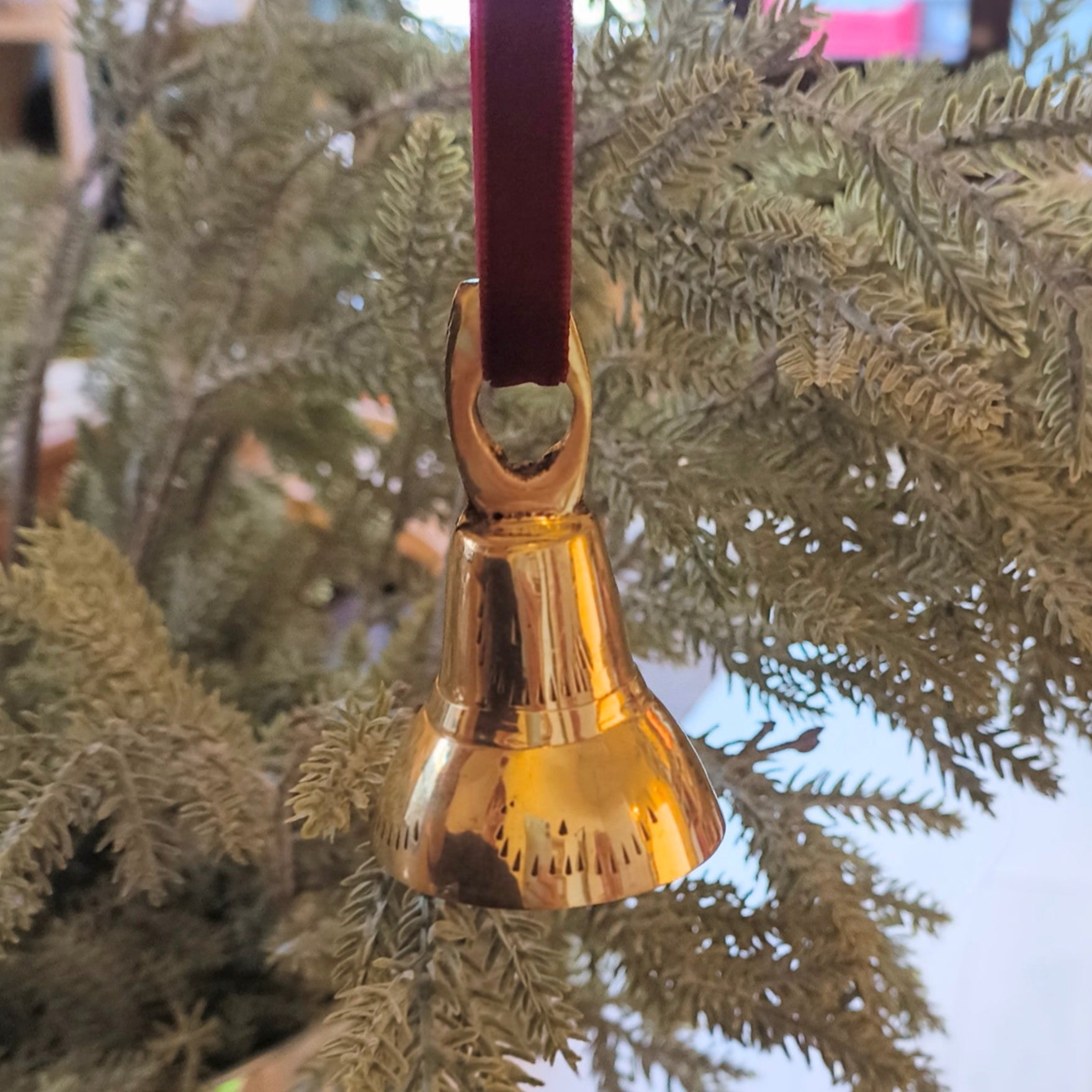 Gold bell ornament hanging from a branch on a wooden surface