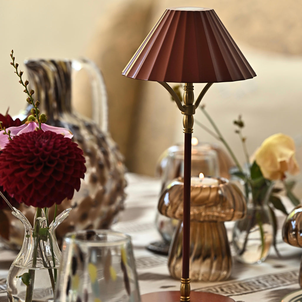 Decorative table lamp with a brown pleated shade on a table with flowers and candles.
