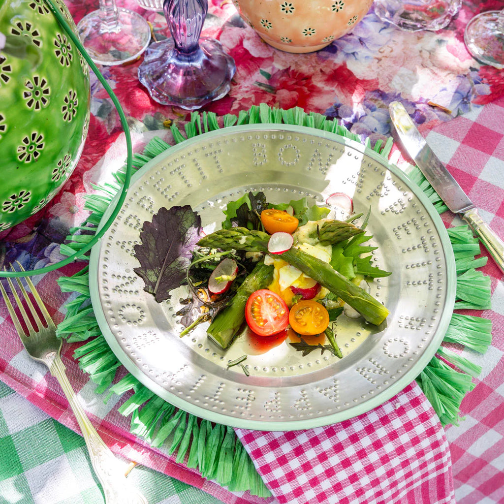 green trimmed metal plate with food on a green placemat on a table setting. 