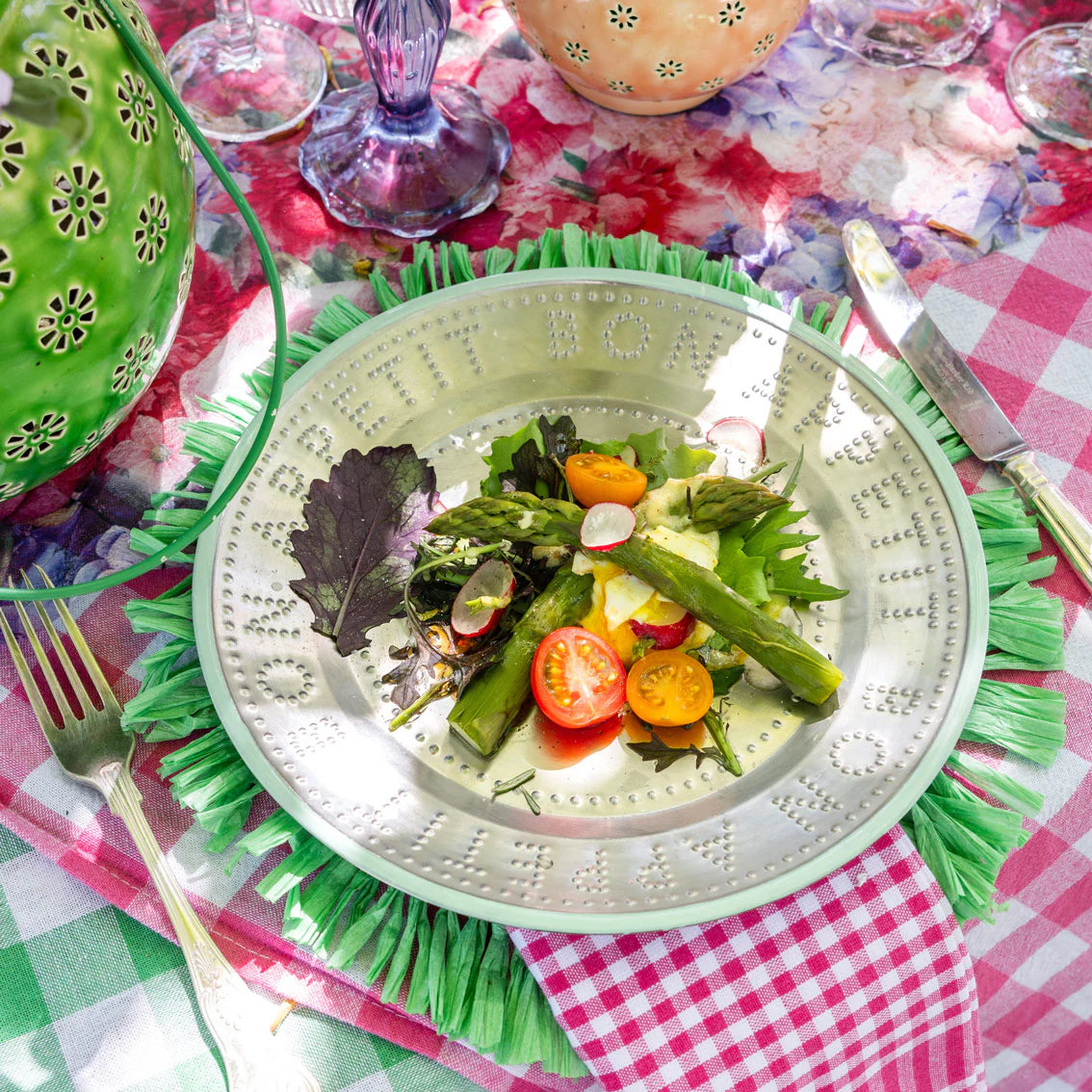 green trimmed metal plate with food on a green placemat on a table setting. 