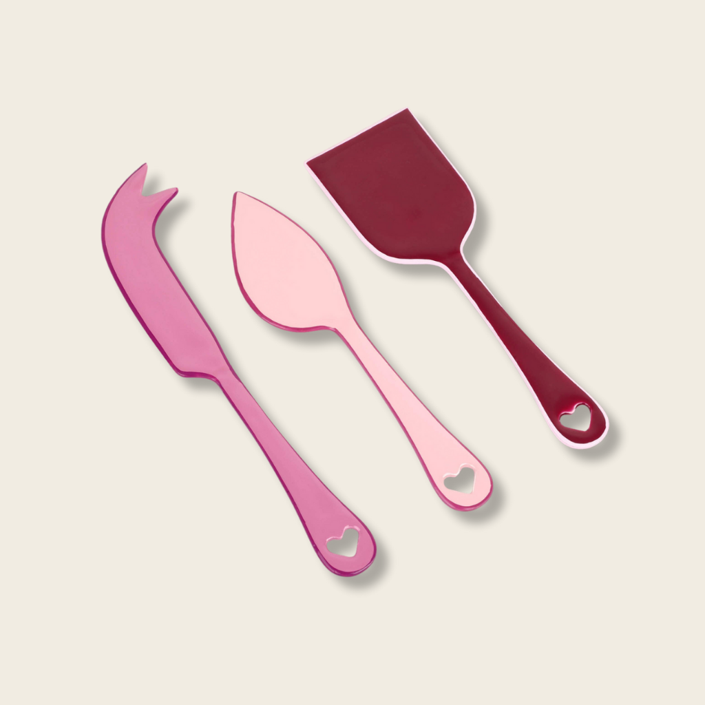 Set of pink and red kitchen utensils with heart designs on a beige background