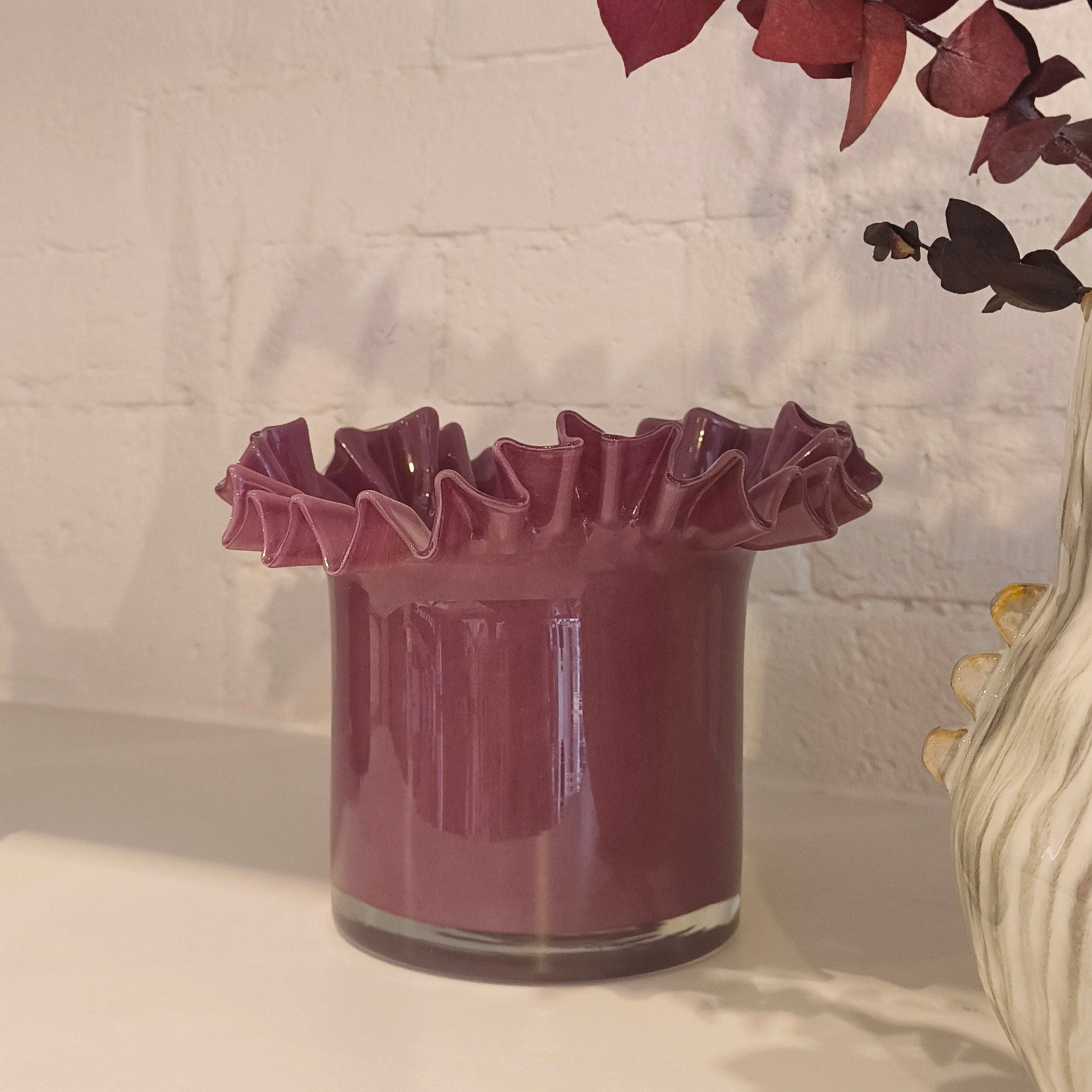 Decorative glass vase with ruffled edges and a vase on a white surface.