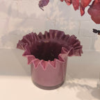 Plum ruffled vase on a white surface with a blurred background