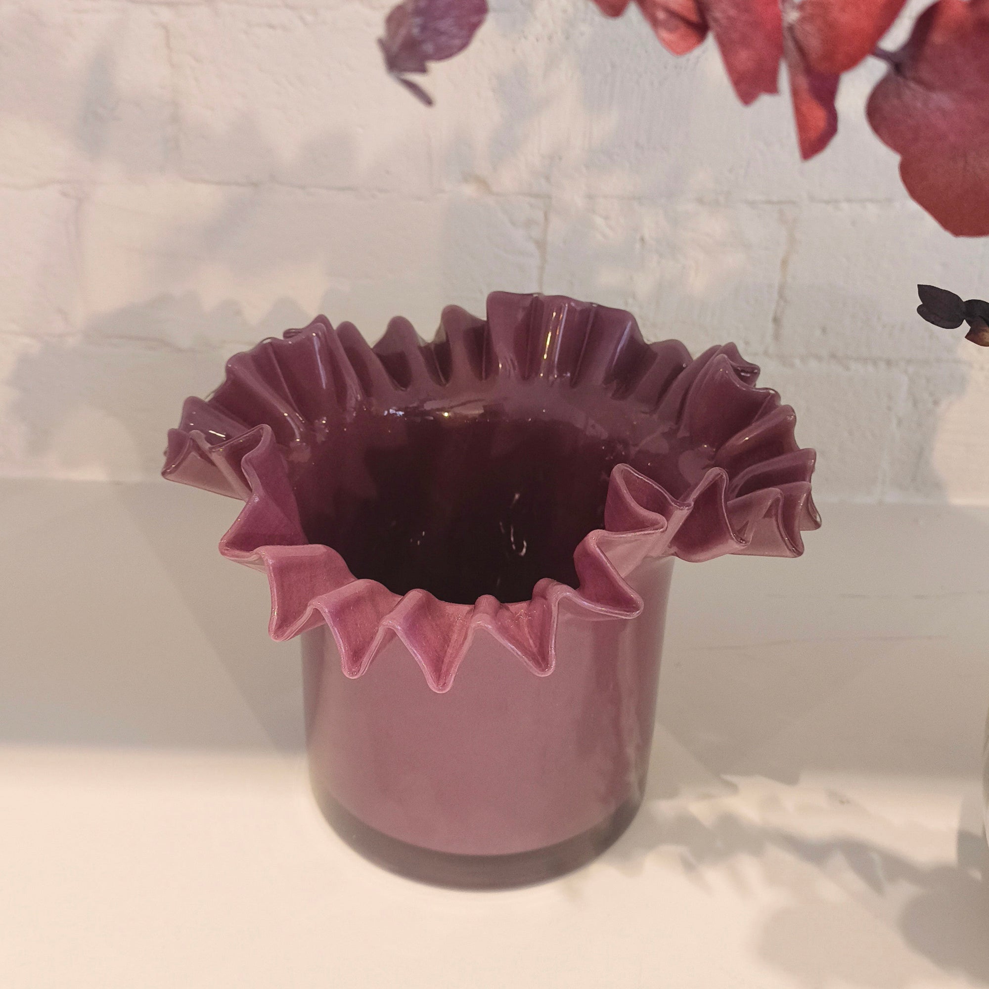 Plum ruffled vase on a white surface with a blurred background