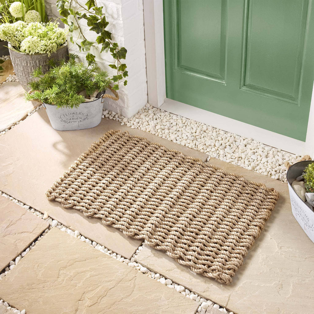 Doormat on a stone patio with a green door and plants in the background