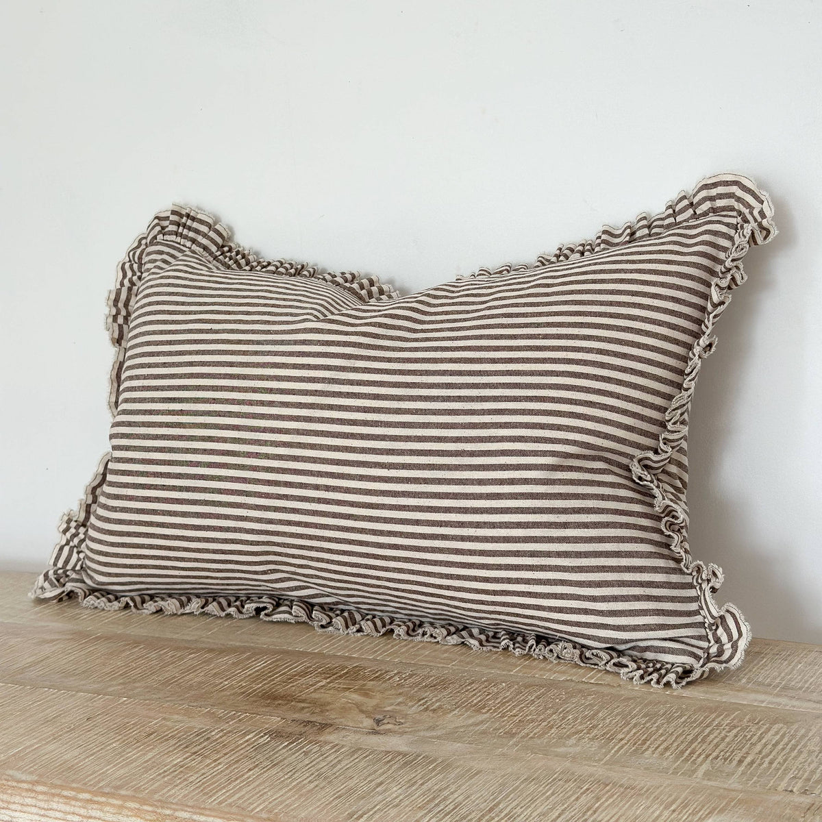 Striped pillow with ruffled edges on a wooden surface against a white wall