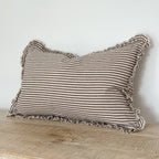 Striped pillow with ruffled edges on a wooden surface against a white wall