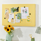 Yellow bulletin board with pinned notes above a desk with a vase of sunflowers and office supplies.
