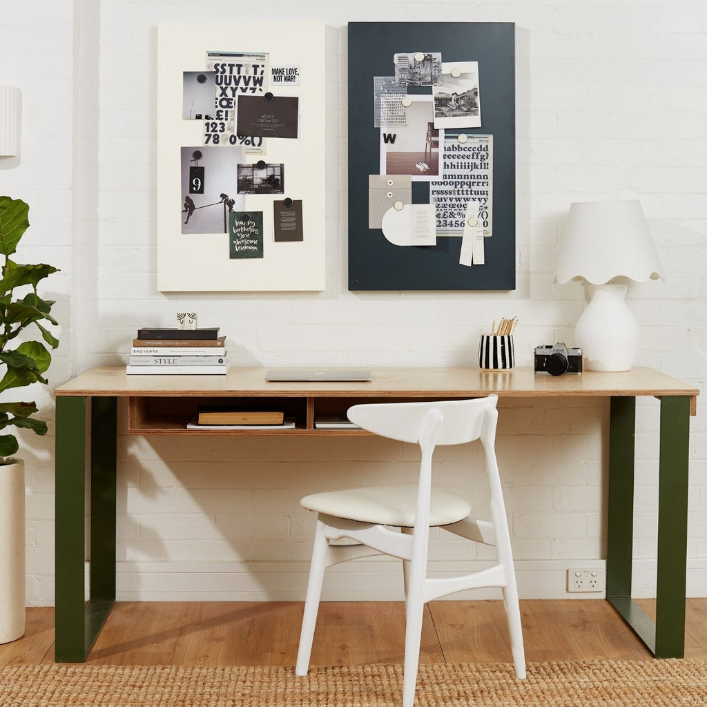 Modern home office with a wooden desk, white chair, and framed artwork on a white wall.