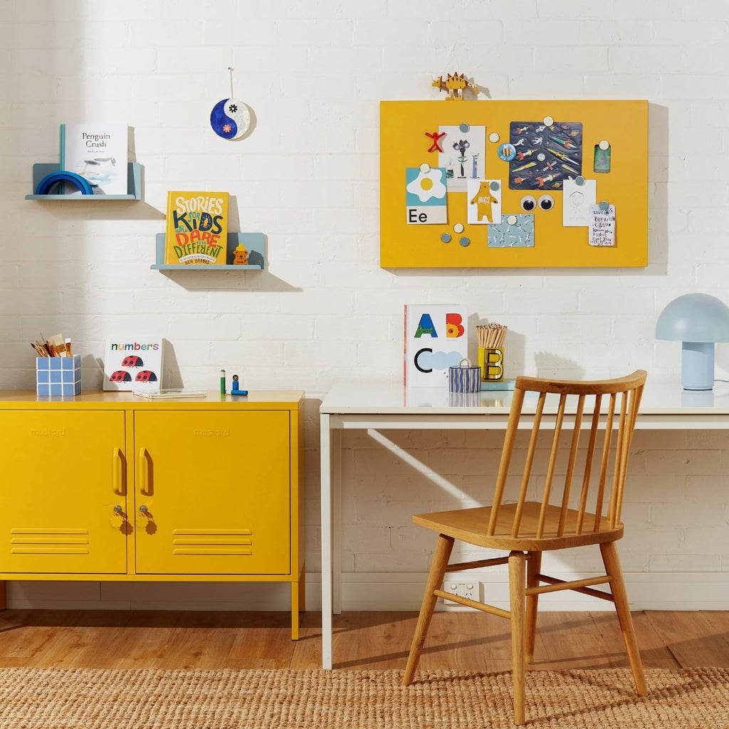 Yellow cabinet, wooden chair, and white desk in a room with a white wall and wooden floor.