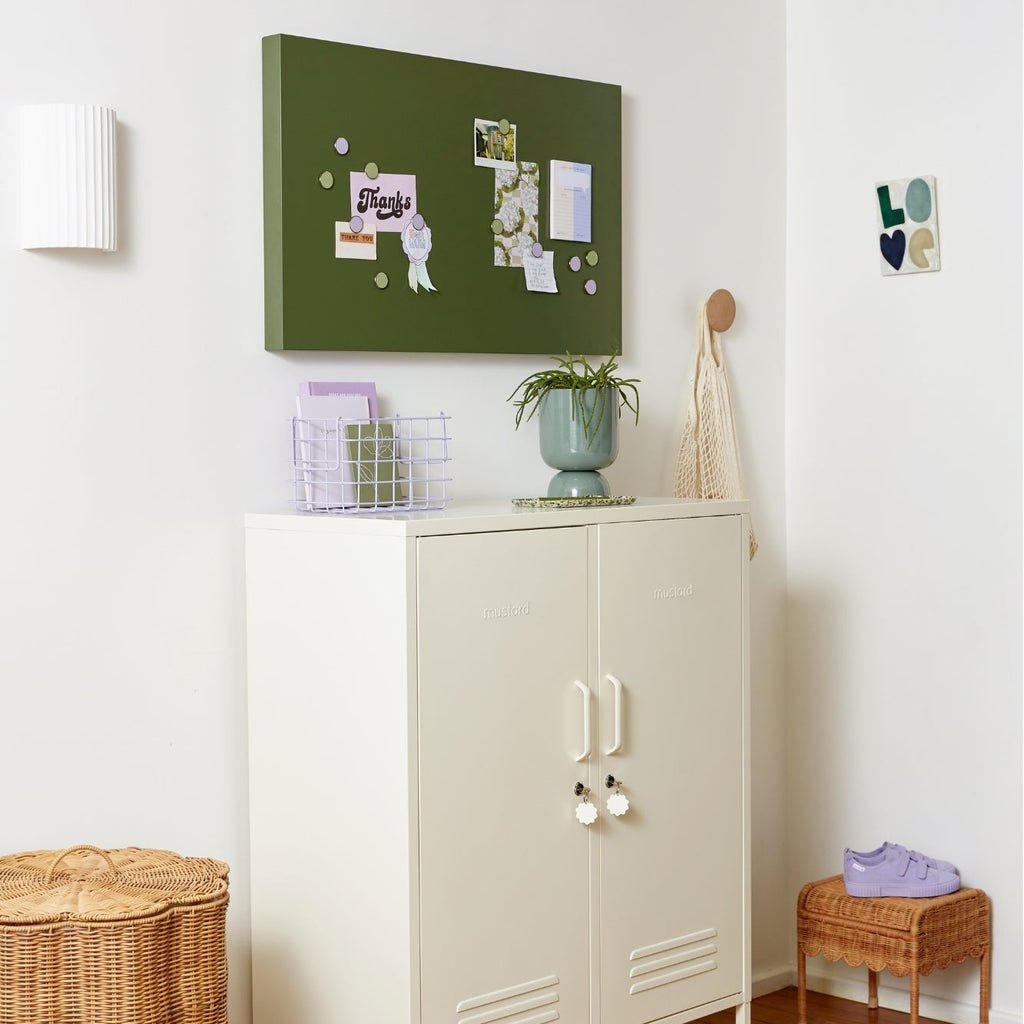 White cabinet with a green bulletin board above it in a room with wooden flooring.