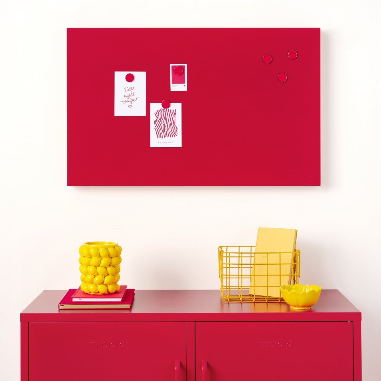 Red magnetic board on a white wall with a red cabinet below displaying yellow decorative items.