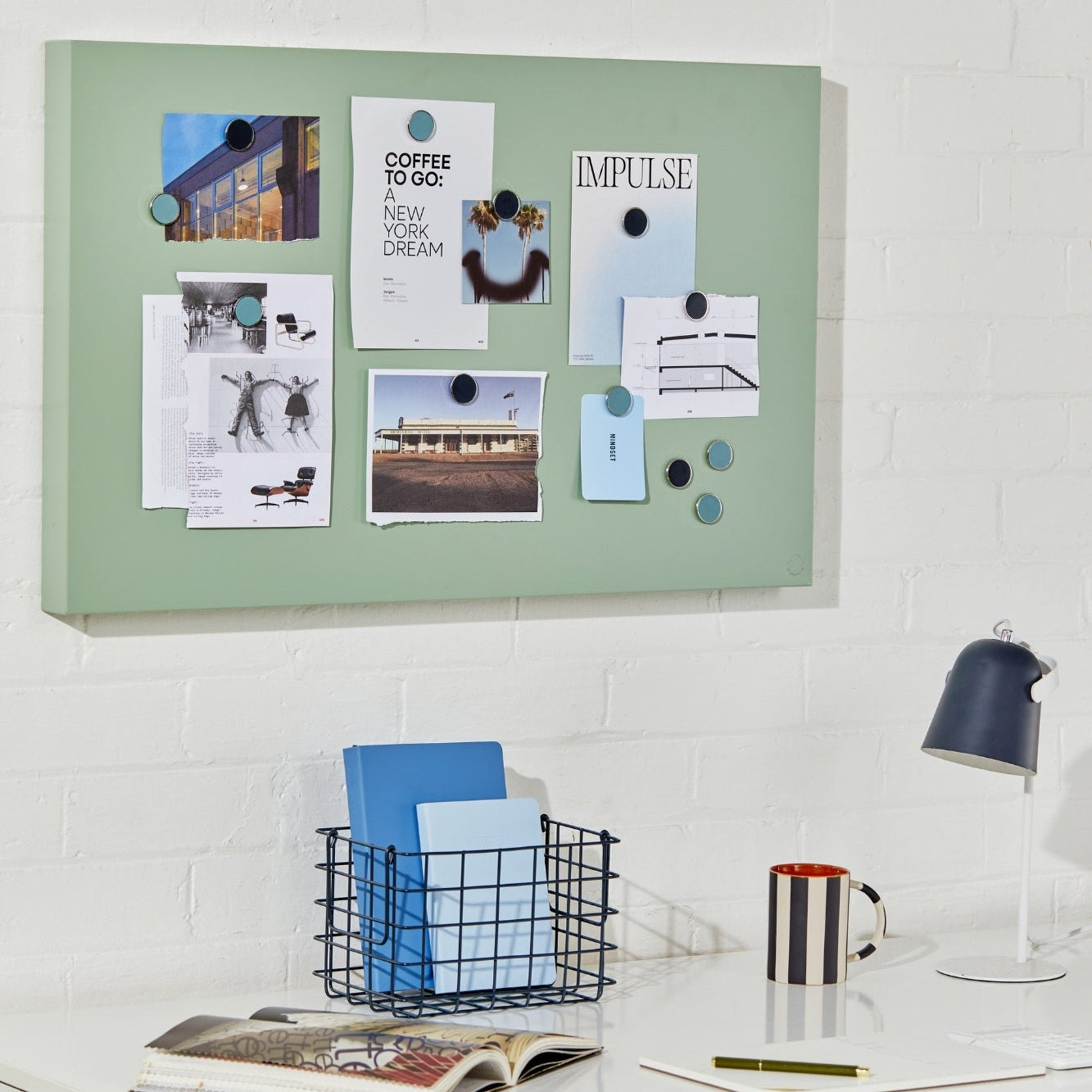 Green magnetic notice board on a white wall above a desk with office supplies.