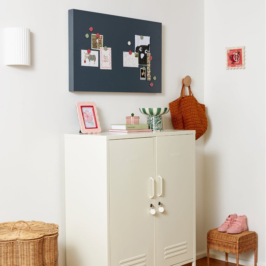 White cabinet with a basket underneath, wicker chair, and decorative items on a white wall.
