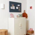 White cabinet with a basket underneath, wicker chair, and decorative items on a white wall.