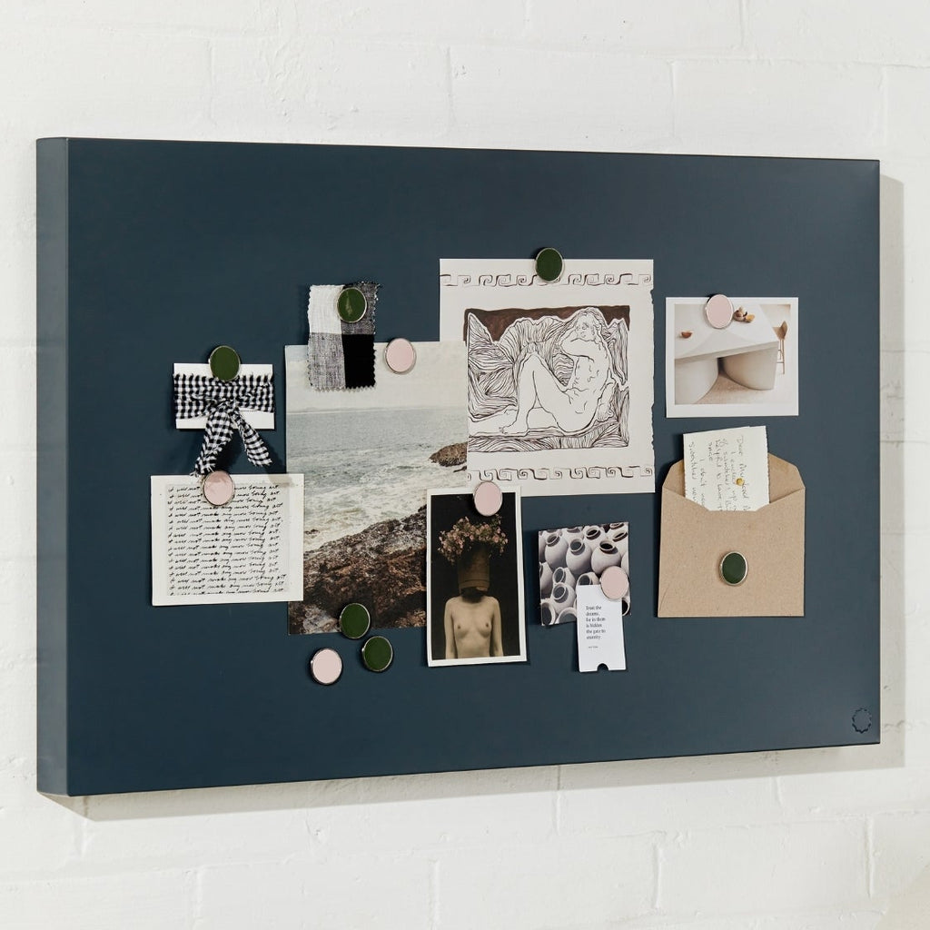 charcoal bulletin board with pinned photos and notes on a white wall above a desk.