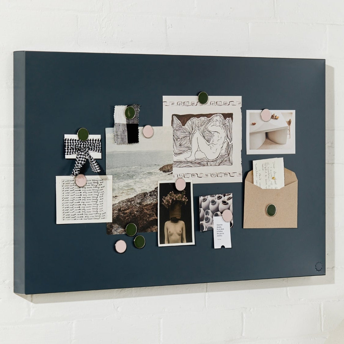 charcoal bulletin board with pinned photos and notes on a white wall above a desk.