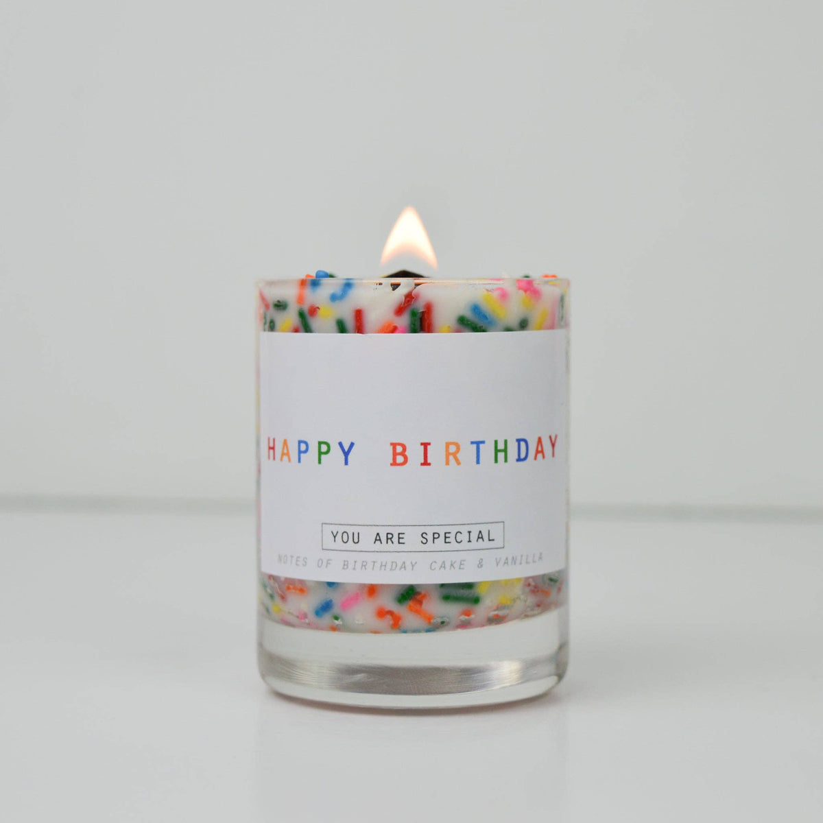 Candle with colorful sprinkles and 'Happy Birthday' label on a white background