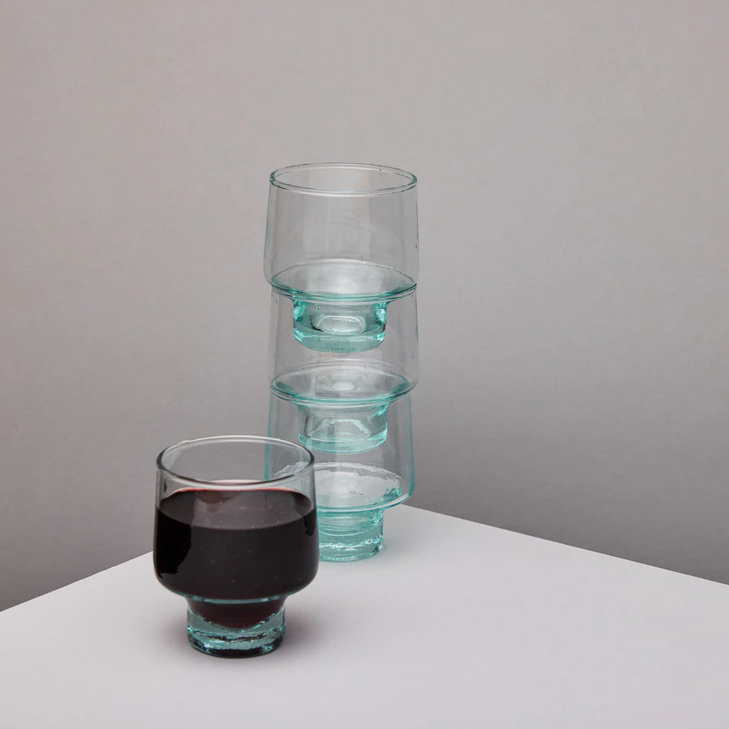 Set of clear glass tumblers with one filled with red wine on a neutral background