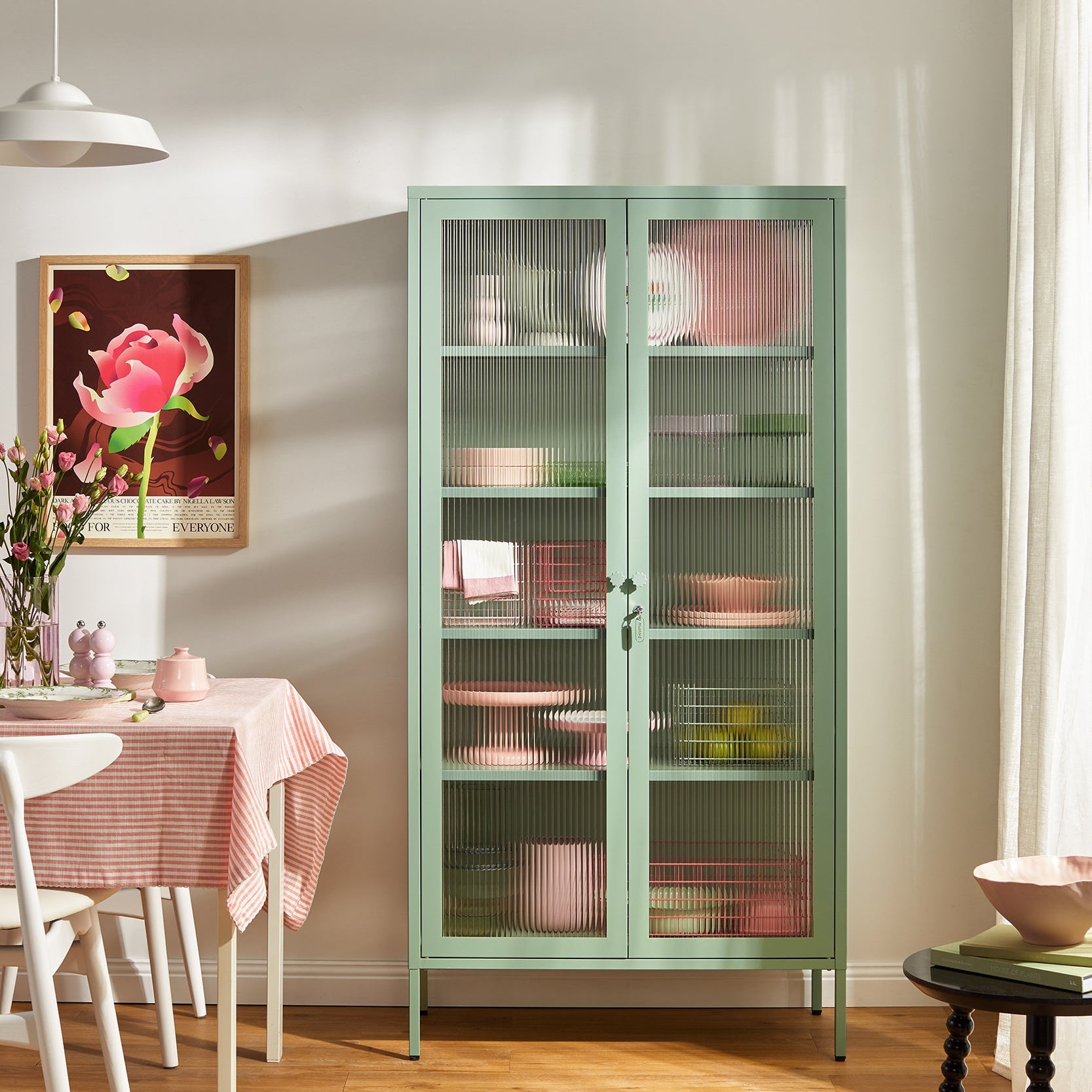 Green glass-front cabinet in a room with a table and decor items.