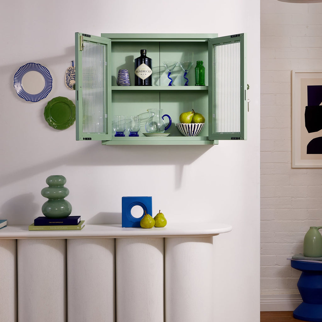 Green wall-mounted cabinet with decorative items in a room with white walls and wooden floor.