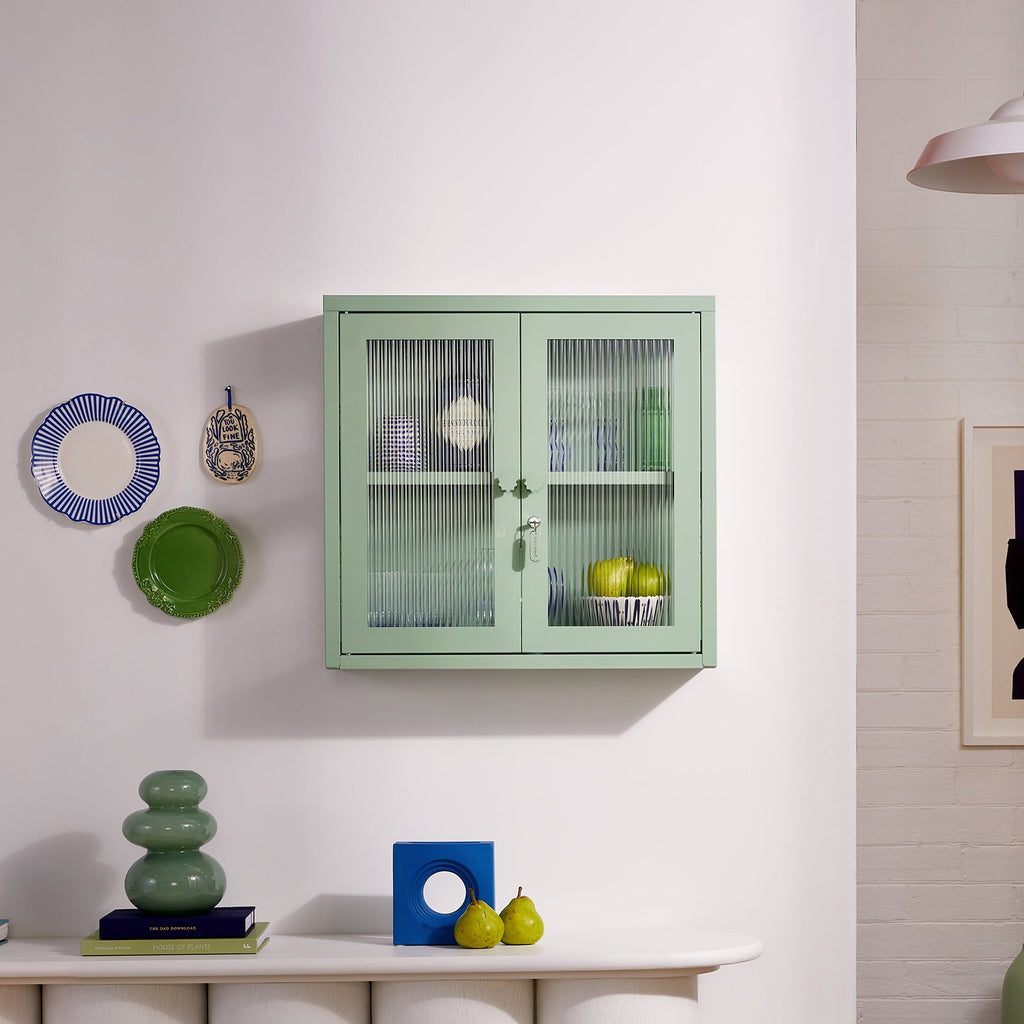 Green cabinet on a white wall with decorative items around