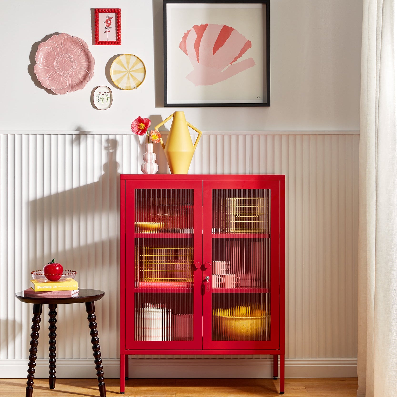 Red cabinet with glass doors in a room with decorative items on the wall.