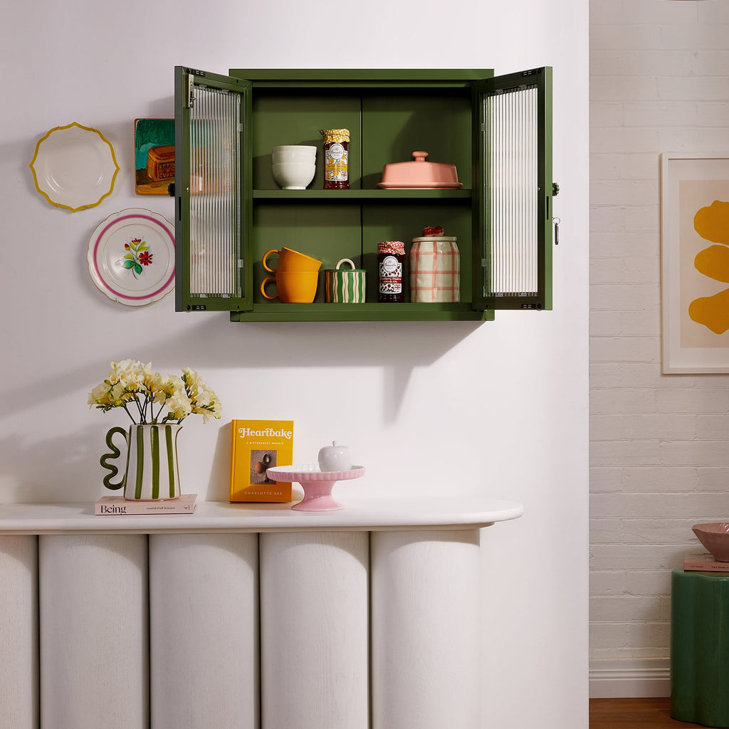 Green wall-mounted cabinet with decorative items in a room with white walls and wooden floor.