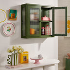 Green wall-mounted cabinet with open doors displaying items, placed on a white shelf against a white wall.