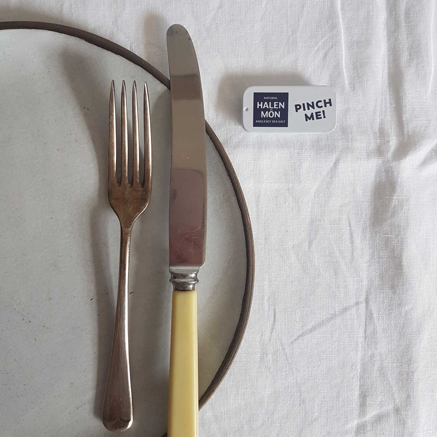 Fork and knife on a plate with a 'Pinch Me' card on a white fabric background
