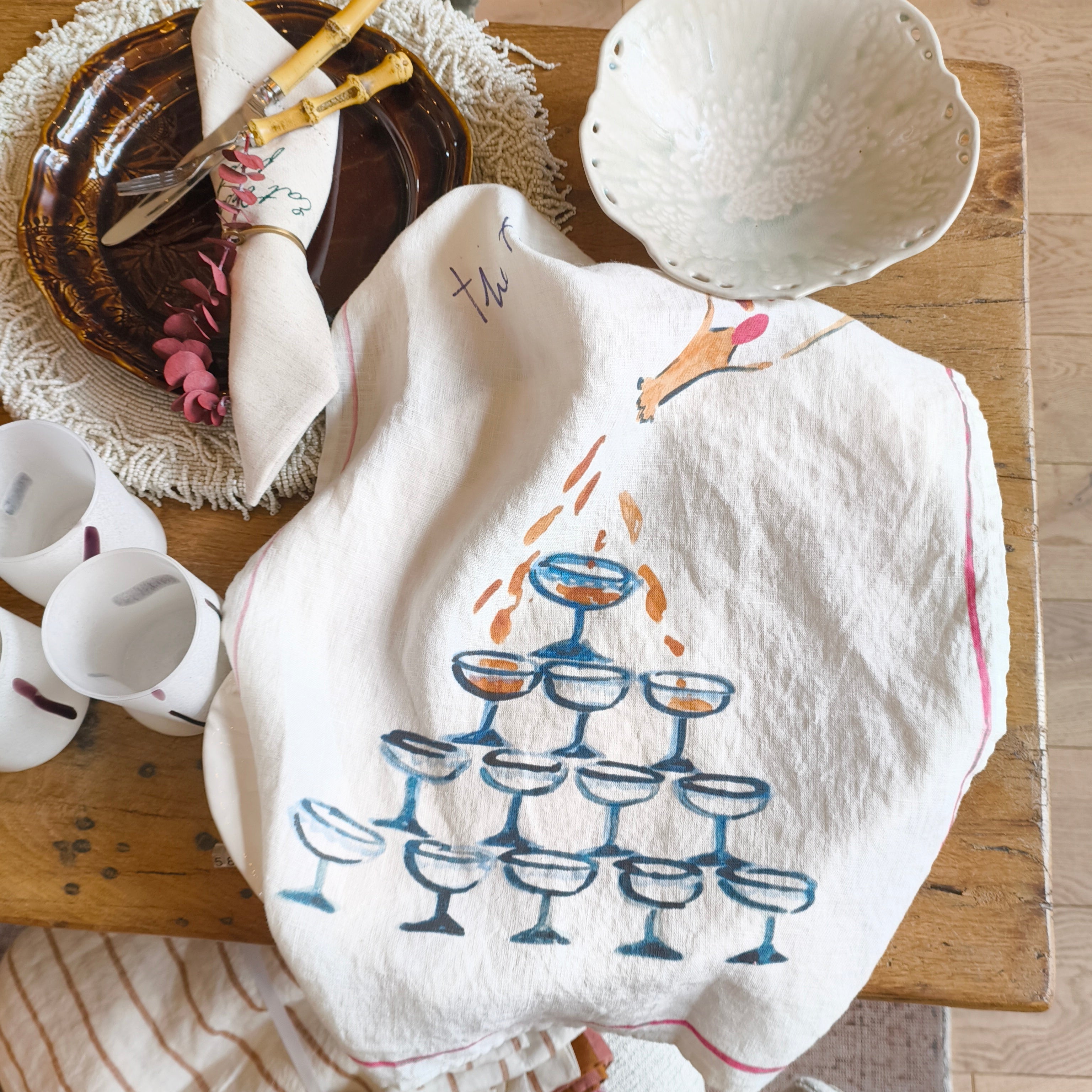 Decorative towel with a glass design on a wooden table with mugs and a bowl.
