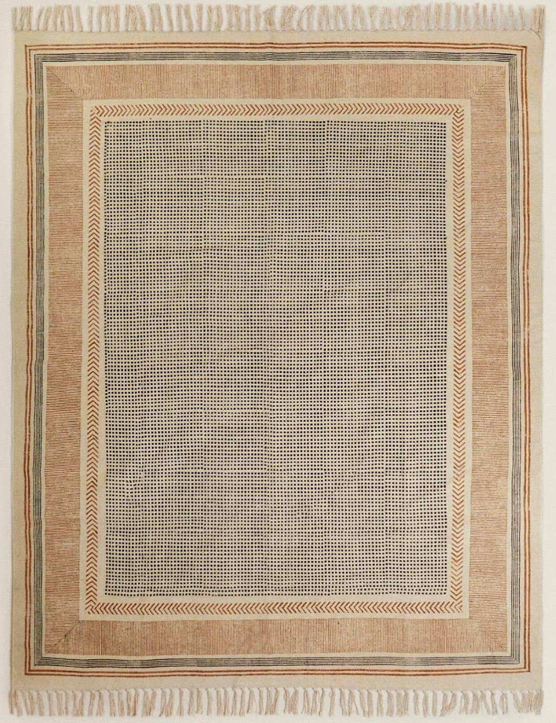 Close-up view of a flatweave rug with a hand-knotted texture, predominantly in a cream color with a rust-colored area, placed on a wooden floor beside a white curtain.