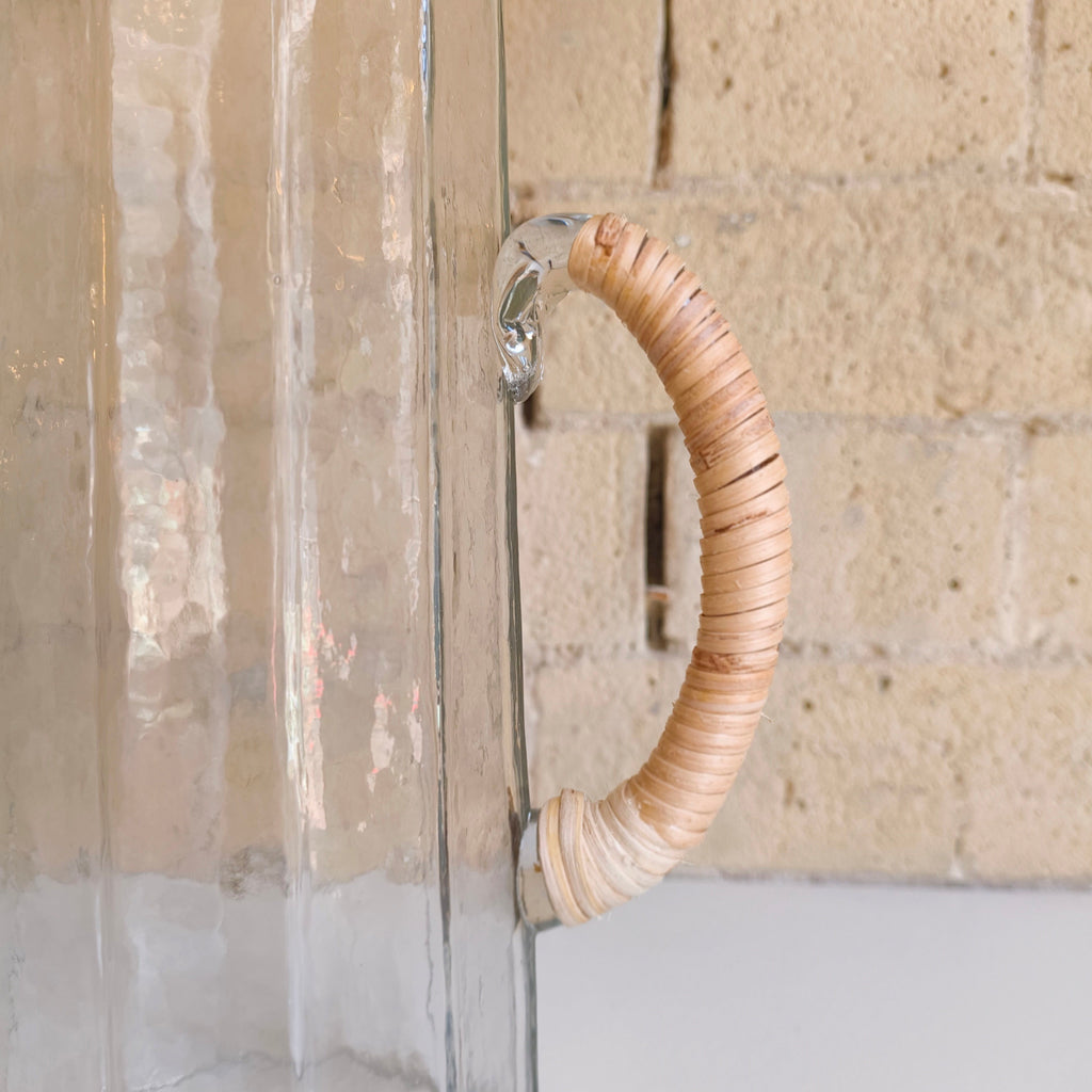 Clear glass vase with woven wooden handle against a stone wall background