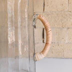 Clear glass vase with woven wooden handle against a stone wall background