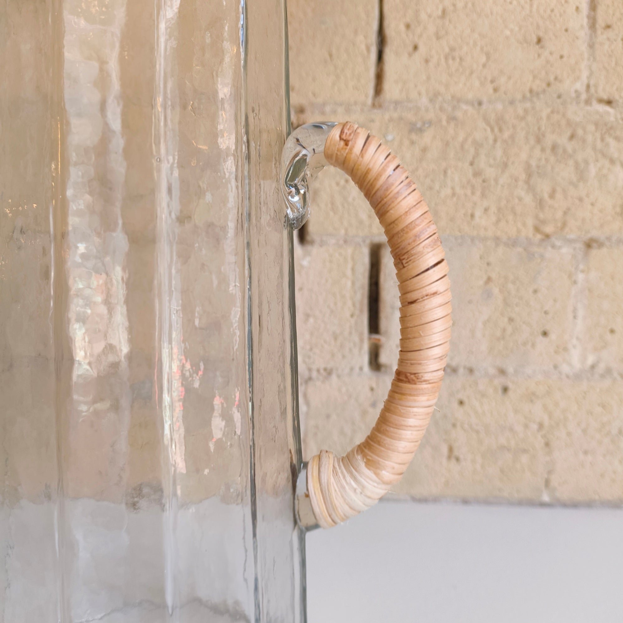 Clear glass vase with woven wooden handle against a stone wall background