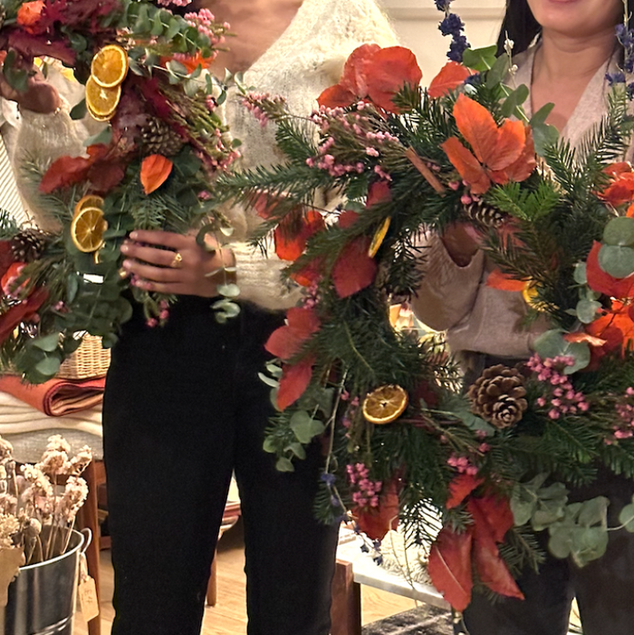 Two people holding large floral wreaths with decorative elements indoors.