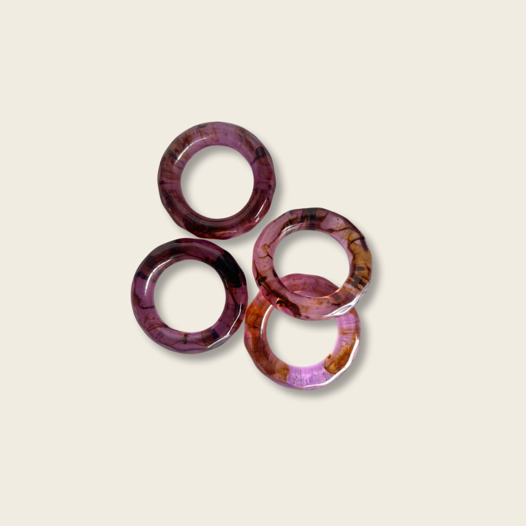 four acrylic napkin rings in amethyst colour on a beige background