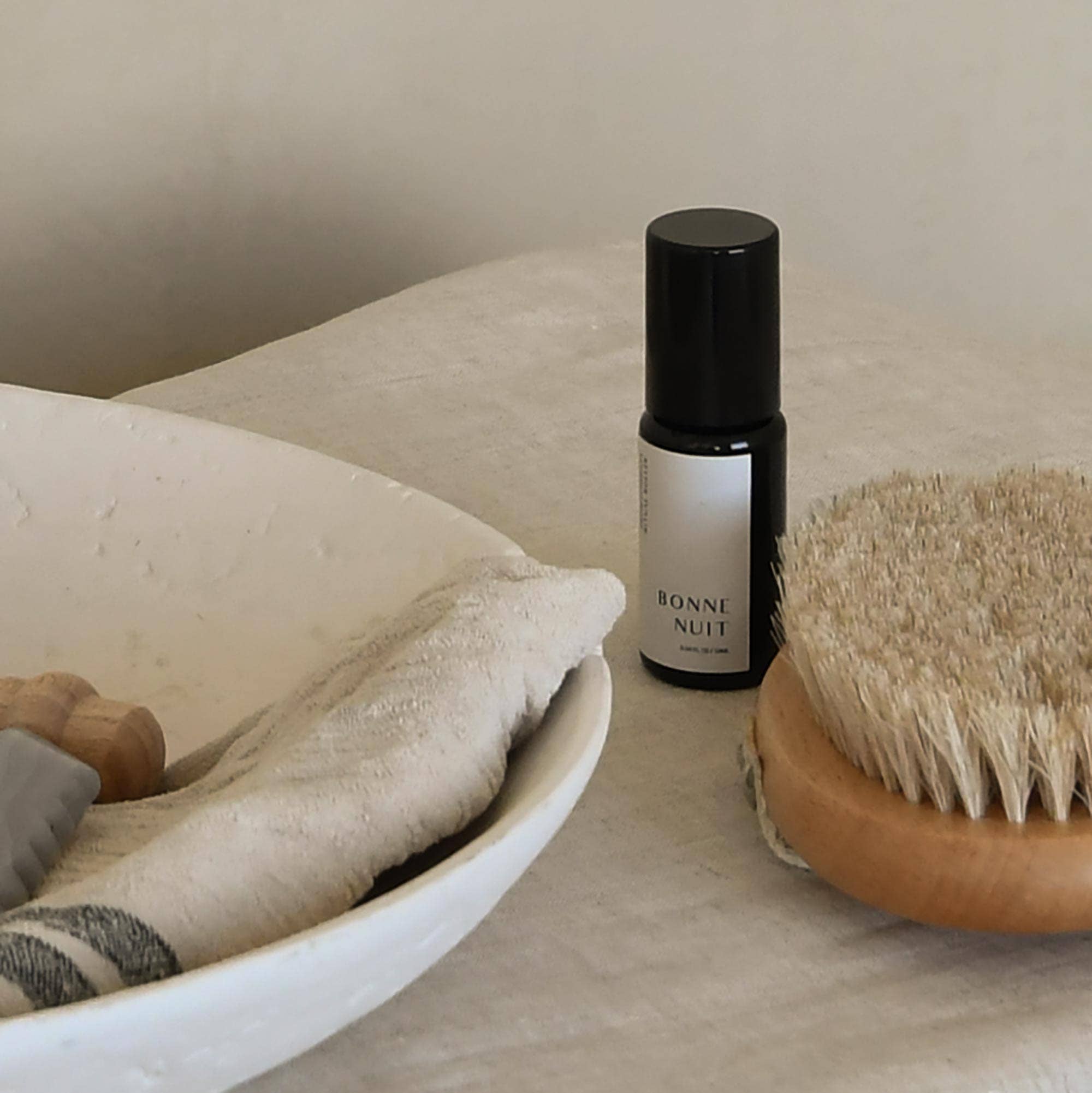 Roller bottle labeled 'Bonne Nuit' next to a body brush on a neutral surface