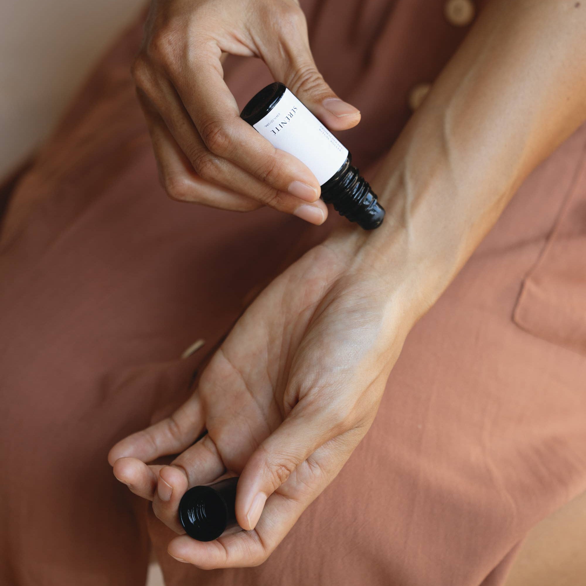 Person applying a black dropper bottle to their wrist.