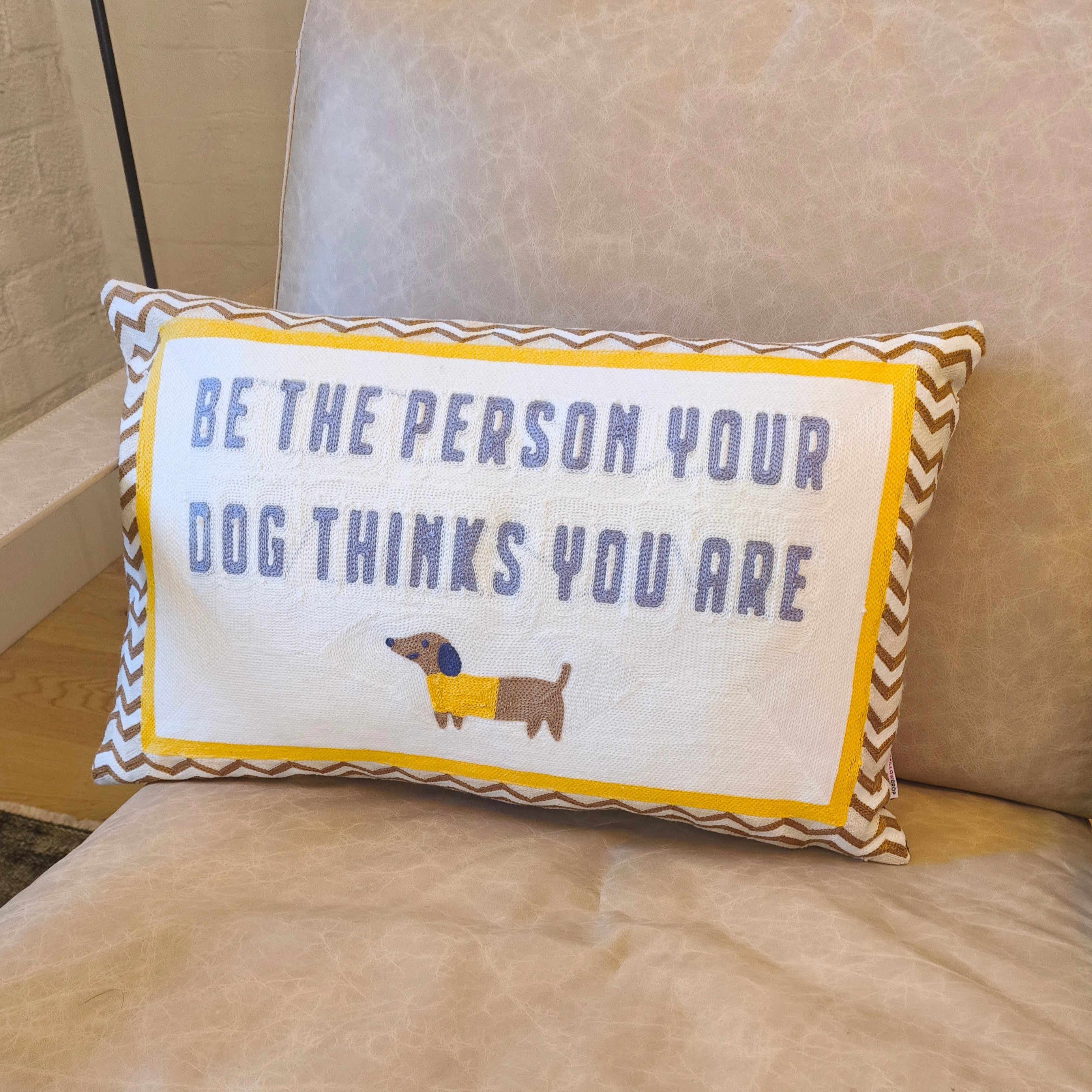 Decorative pillow with a dachshund illustration and text on a beige couch.