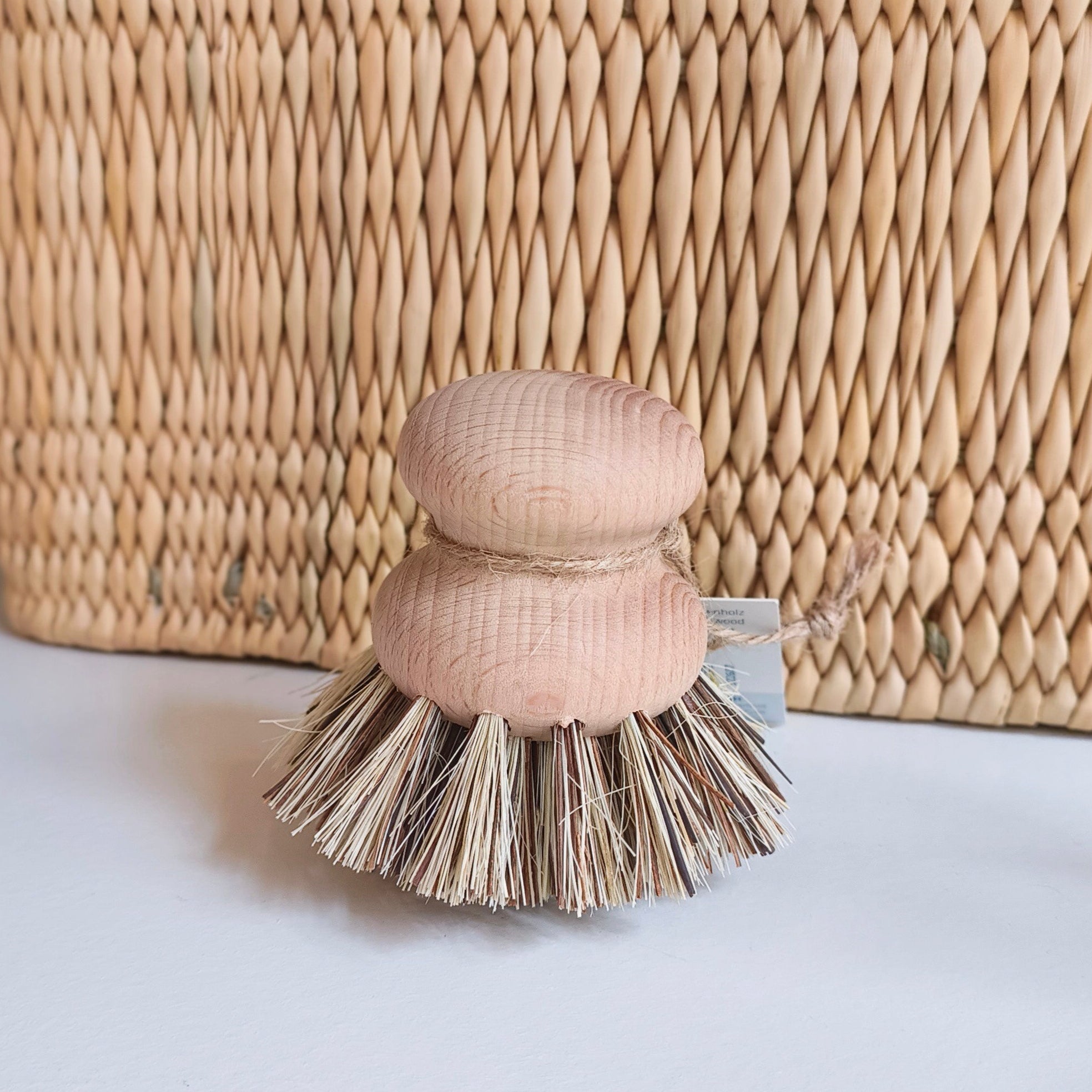 Small brush with wooden handle and bristle head on a white surface, with a woven basket in the background.