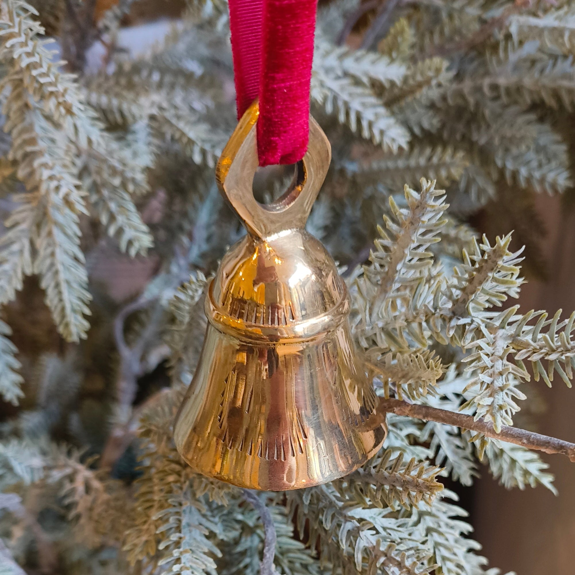 Gold bell ornament on a branch with a red ribbon against a Christmas tree background