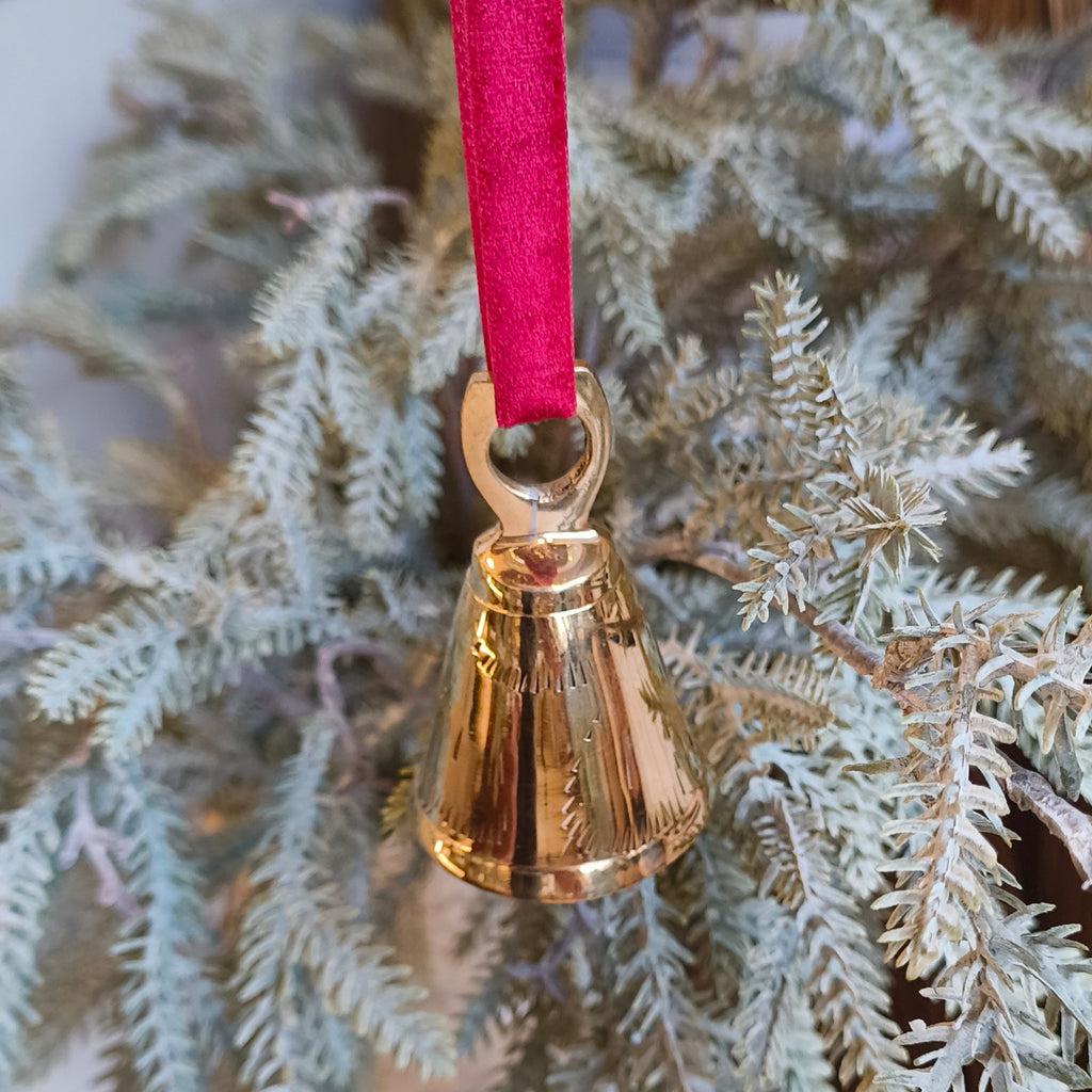 Gold bell ornament on a red ribbon hanging from a Christmas tree.