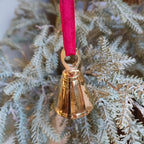 Gold bell ornament on a red ribbon hanging from a Christmas tree.
