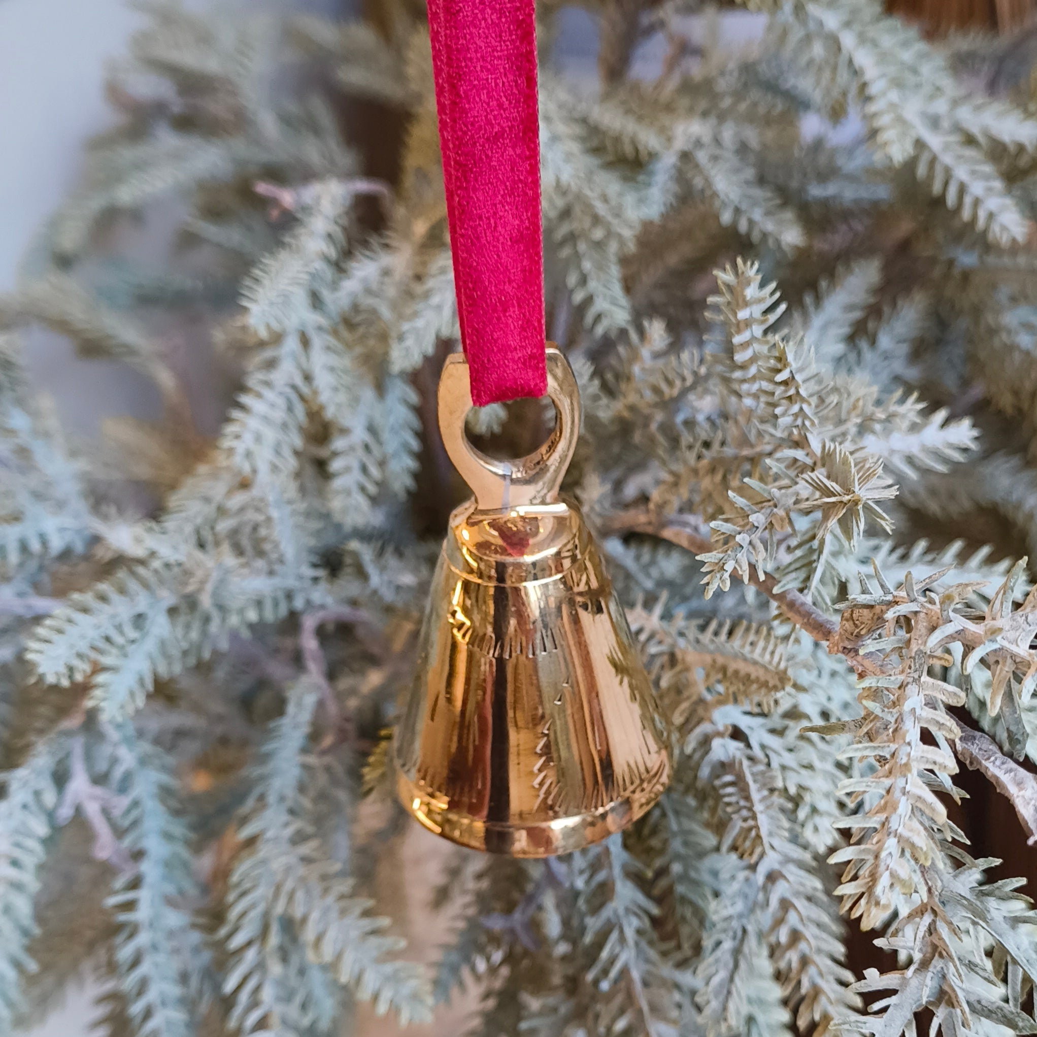 Gold bell ornament on a red ribbon hanging from a Christmas tree.