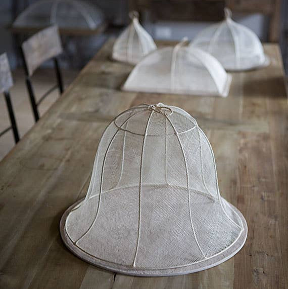 White mesh cloche on a wooden table with blurred background