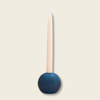 tall white taper candle in a black stone ball candle holder with a beige background